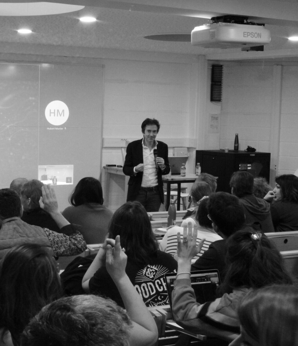 Groupe de personnes assises dans une salle de présentation, en noir et blanc.