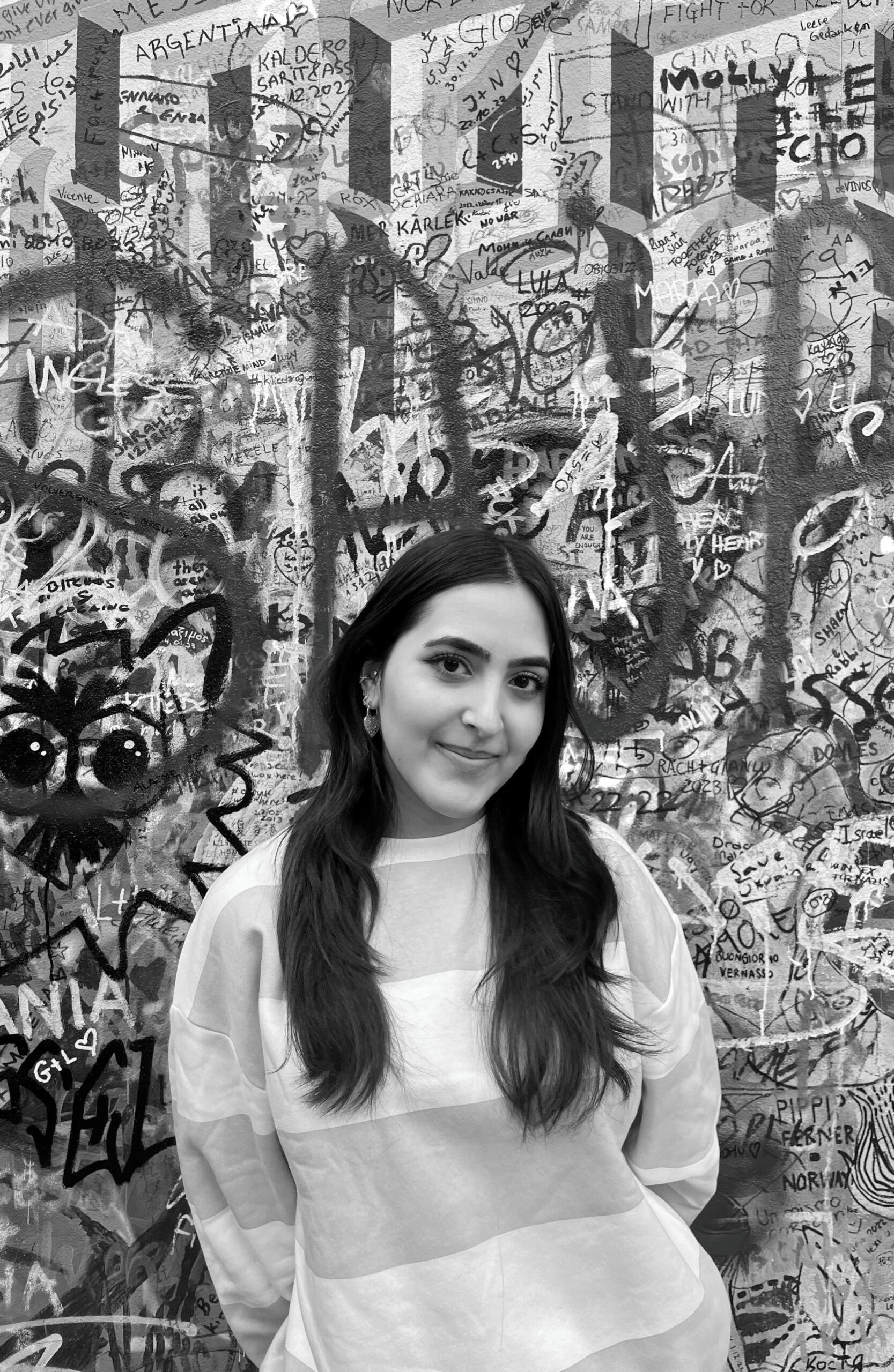 Portrait en noir et blanc d’une étudiante devant un mur recouvert d’illustrations.
