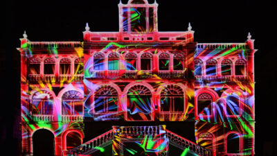 Projection monumentale de lumières multicolores sur la façade d’un bâtiment historique, transformée en œuvre immersive grâce au mapping vidéo et aux effets visuels numériques.