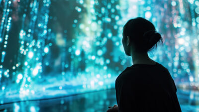 Personne observant une installation immersive composée de milliers de points lumineux bleus suspendus, créant une ambiance futuriste et contemplative inspirée de l’art numérique.