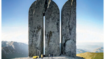 Affiche publicitaire pour une marque d’outdoor montrant une imposante formation rocheuse sculptée en forme de lettres monumentales au sommet d’une montagne, symbolisant l’exploration et le dépassement de soi.