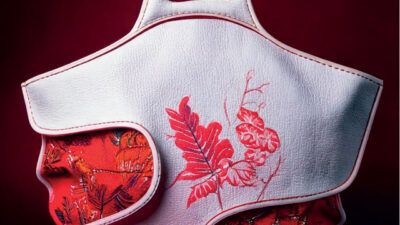 Sac à main blanc au design sculptural et asymétrique, orné de broderies florales rouges et de découpes révélant un textile imprimé, photographié sur fond rouge dans un univers de mode et d’artisanat contemporain.
