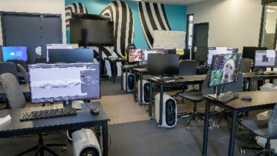 Salle de création 3D avec postes informatiques et écrans affichant des projets étudiants