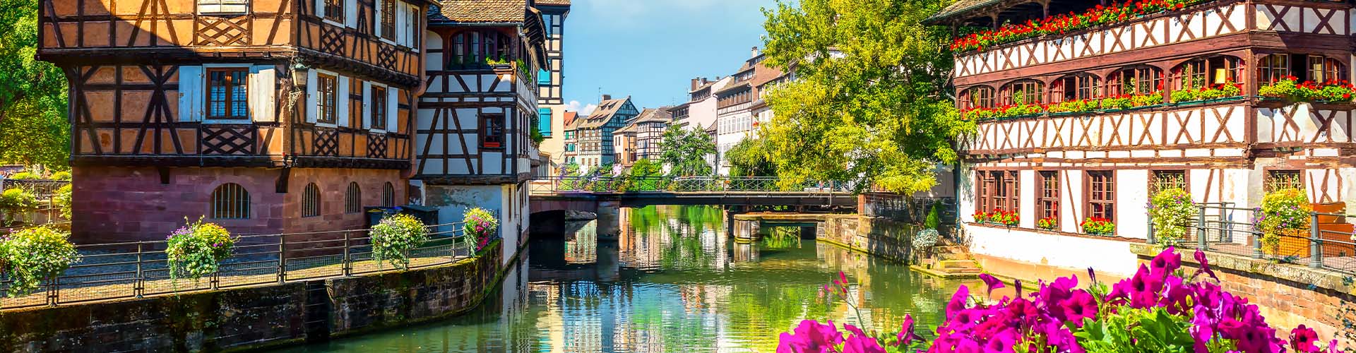 Vue pittoresque du quartier de la Petite France à Strasbourg avec maisons à colombages, canal fleuri et architecture alsacienne traditionnelle sous un ciel ensoleillé