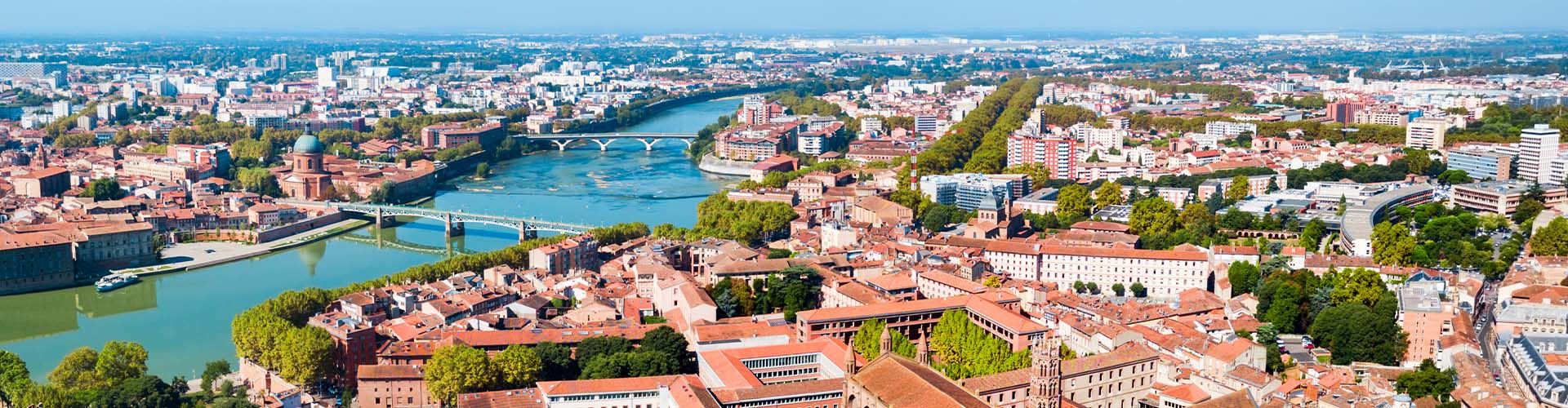 Vue aérienne de Toulouse avec la Garonne, ses ponts historiques et les toits en terre cuite emblématiques du centre-ville sous un ciel dégagé
