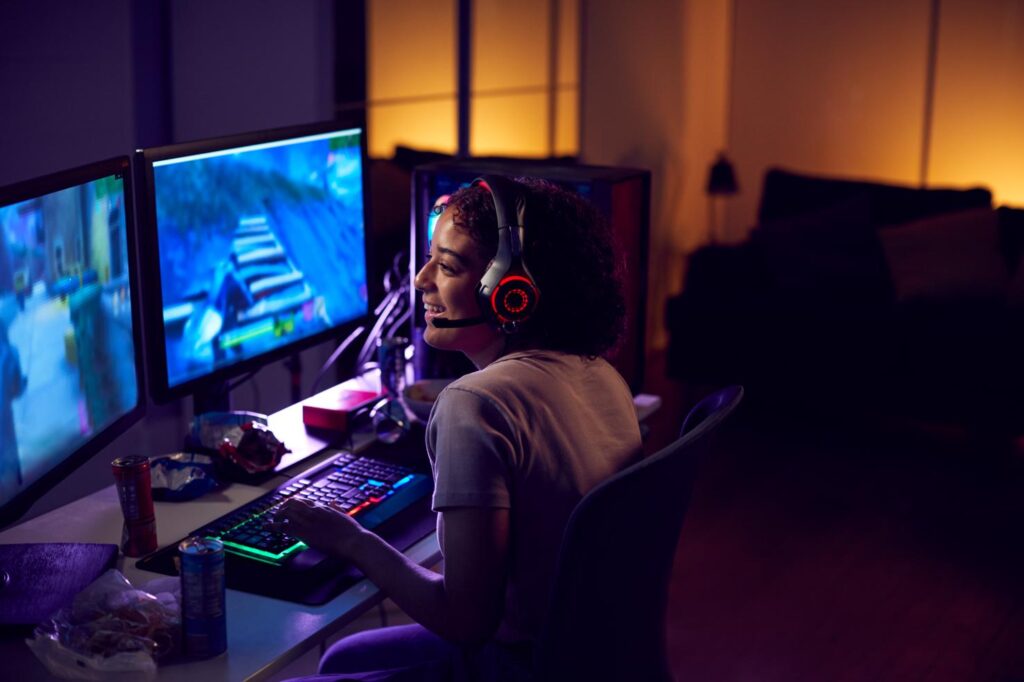 Jeune gameuse portant un casque gaming jouant à un jeu vidéo sur PC dans un setup esport avec éclairage LED.