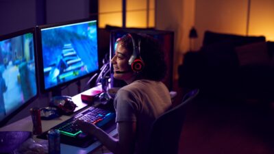 Jeune gameuse portant un casque gaming jouant à un jeu vidéo sur PC dans un setup esport avec éclairage LED.