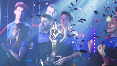 Équipe gagnante levant un trophée lors d’un tournoi esport professionnel avec confettis et éclairages scéniques.