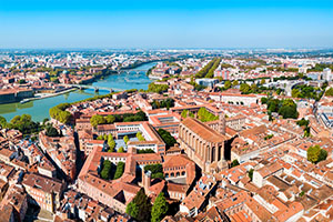 Vue aérienne de Toulouse avec la Garonne, ses ponts historiques et les toits en terre cuite emblématiques du centre-ville sous un ciel dégagé