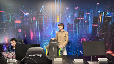 Étudiant dans une salle gaming e-artsup avec fond cyberpunk lumineux et postes informatiques dédiés à la création numérique