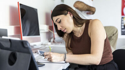 Étudiante prenant des notes et travaillant sur un projet créatif en salle informatique