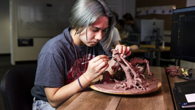 Étudiante sculptant une créature fantastique en argile lors d’un atelier de character design et modelage