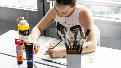 Étudiante réalisant des croquis traditionnels avec peinture et matériel artistique sur table de travail