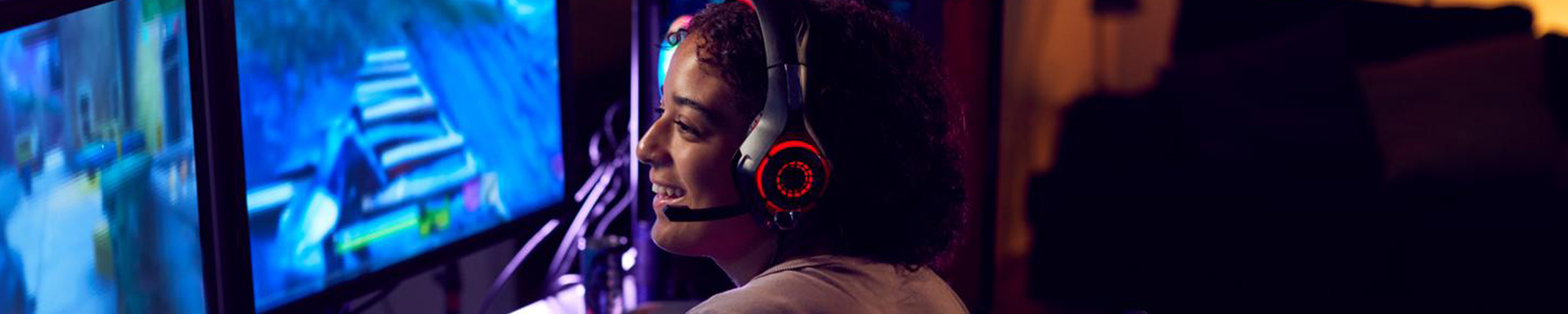 Jeune gameuse portant un casque gaming jouant à un jeu vidéo sur PC dans un setup esport avec éclairage LED.