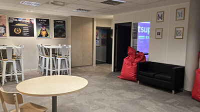 Hall de vie étudiante avec tables hautes, poufs rouges et affiches créatives dans le campus e-artsup Strasbourg