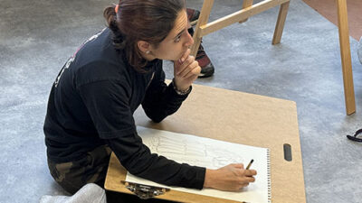Étudiante dessinant une étude d’observation assise au sol dans un atelier artistique e-artsup