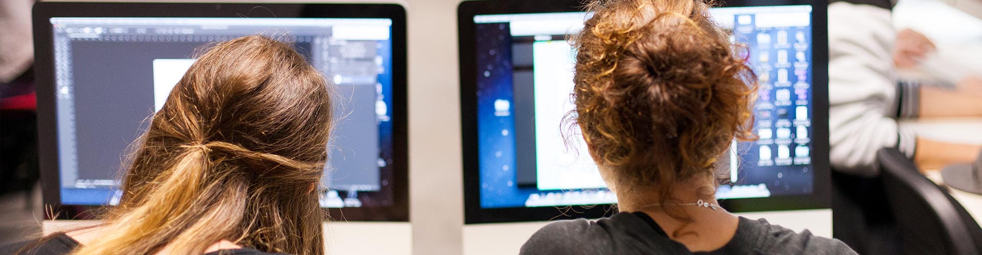 Deux femmes de dos travaillant sur des ordinateurs Apple iMac dans une salle de formation.