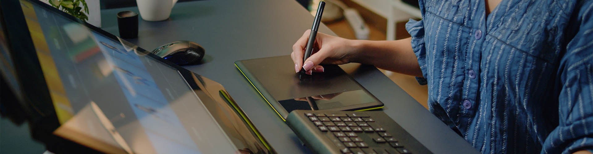 Gros plan sur une graphiste utilisant une tablette graphique à son bureau face à ses écrans d'ordinateur.