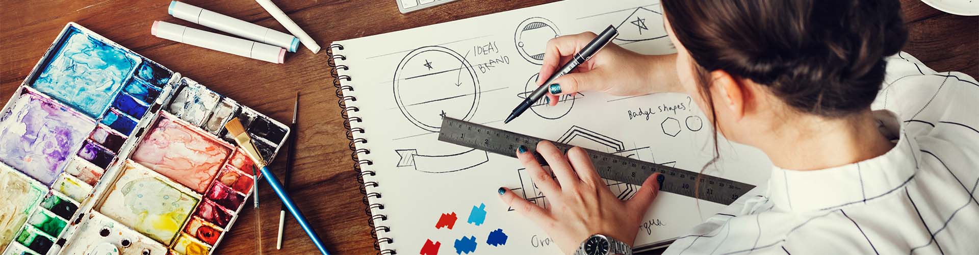 Étudiante ou professionnelle en design graphique travaillant sur la création d'une identité visuelle et de concepts de marque sur un bureau en bois.