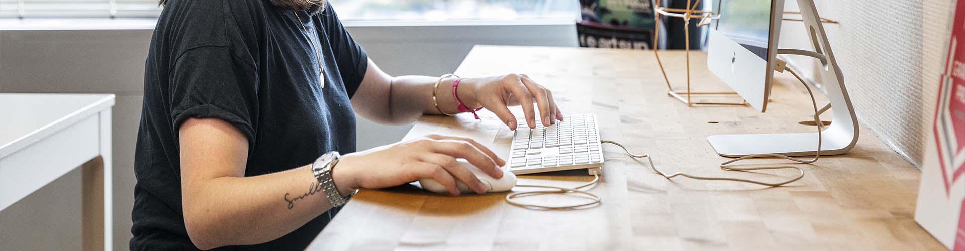Étudiante de l'école e-artsup travaillant sur un ordinateur Apple iMac posé sur un bureau en bois clair.