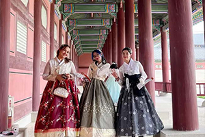 Trois étudiantes internationales portant le Hanbok traditionnel sous les arcades d'un palais en Corée du Sud.