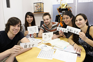 Groupe d'étudiants internationaux souriants montrant des calligraphies japonaises lors d'un cours de langue au Japon.