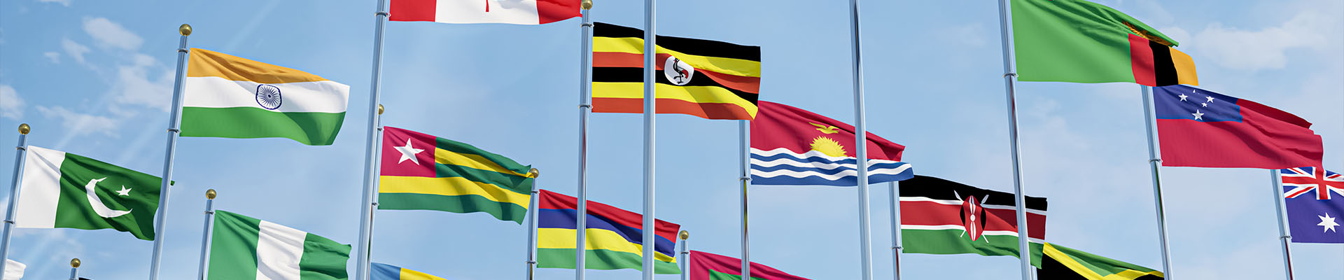 Différents drapeaux du monde flottant sur des mâts alignés sous un ciel bleu ensoleillé.