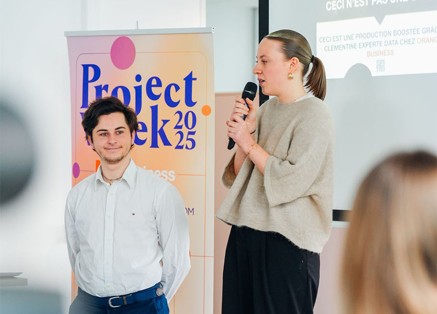 2 étudiants devant un kakémono Project Week 2025 présentant leur projet réalisé en collaboration avec les étudients des écoles ISEG et Epitech, durant la Project Week 2025 à un jury