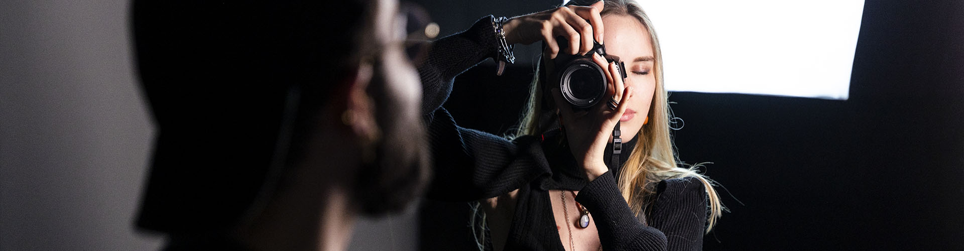 Photographe visant avec son appareil photo reflex ou hybride lors d'un shooting en studio avec éclairage professionnel.
