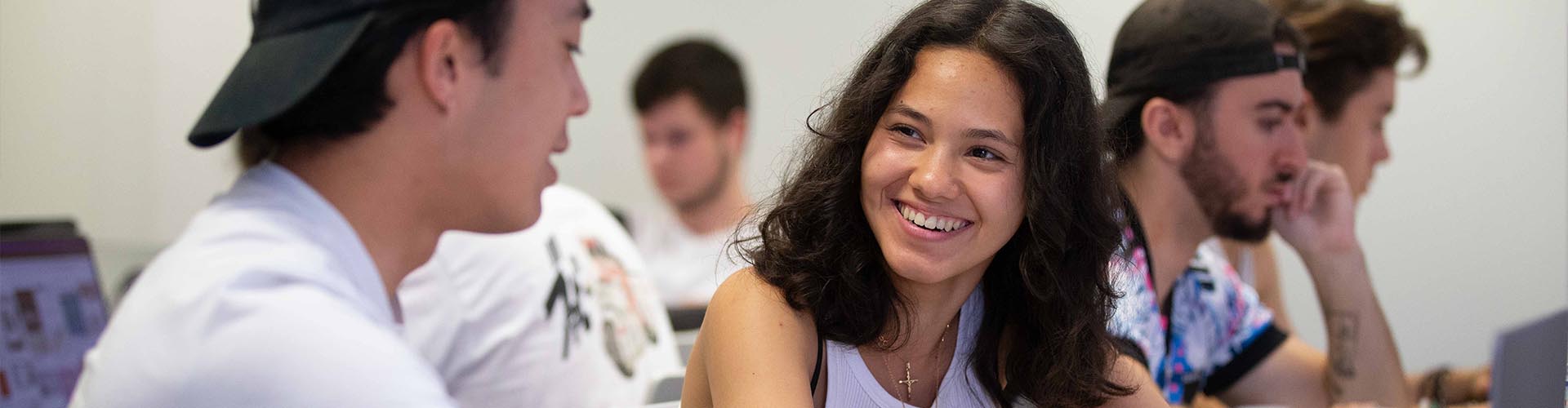 Deux étudiants en école de design e-artsup discutant avec le sourire lors d'un cours sur ordinateur.