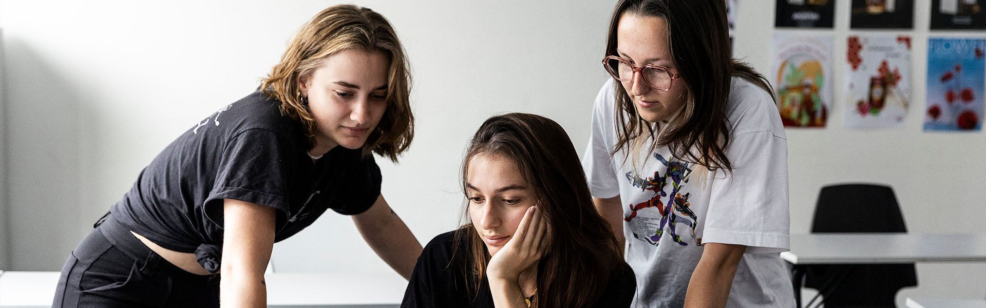 Trois étudiantes en école de création concentrées et collaborant ensemble devant un écran d'ordinateur.