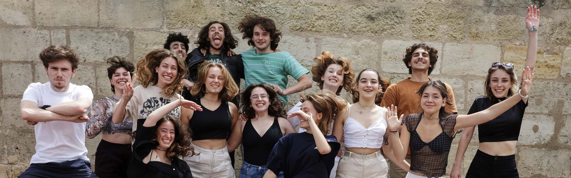 Un groupe d'étudiants de l'école de design e-artsup sautant et souriant ensemble devant un mur en pierre lors d'un projet de groupe.