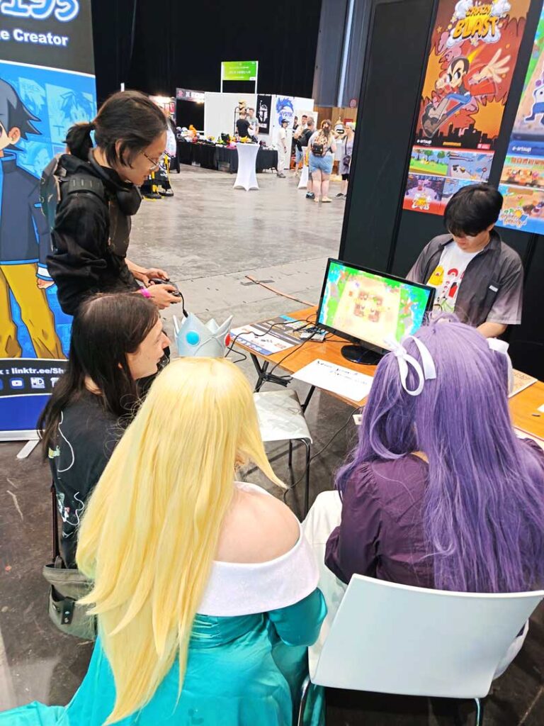 Plusieurs visiteurs réunis autour d’une partie de Musical Sunbeds sur le stand de jeux indépendants à Japan Expo.