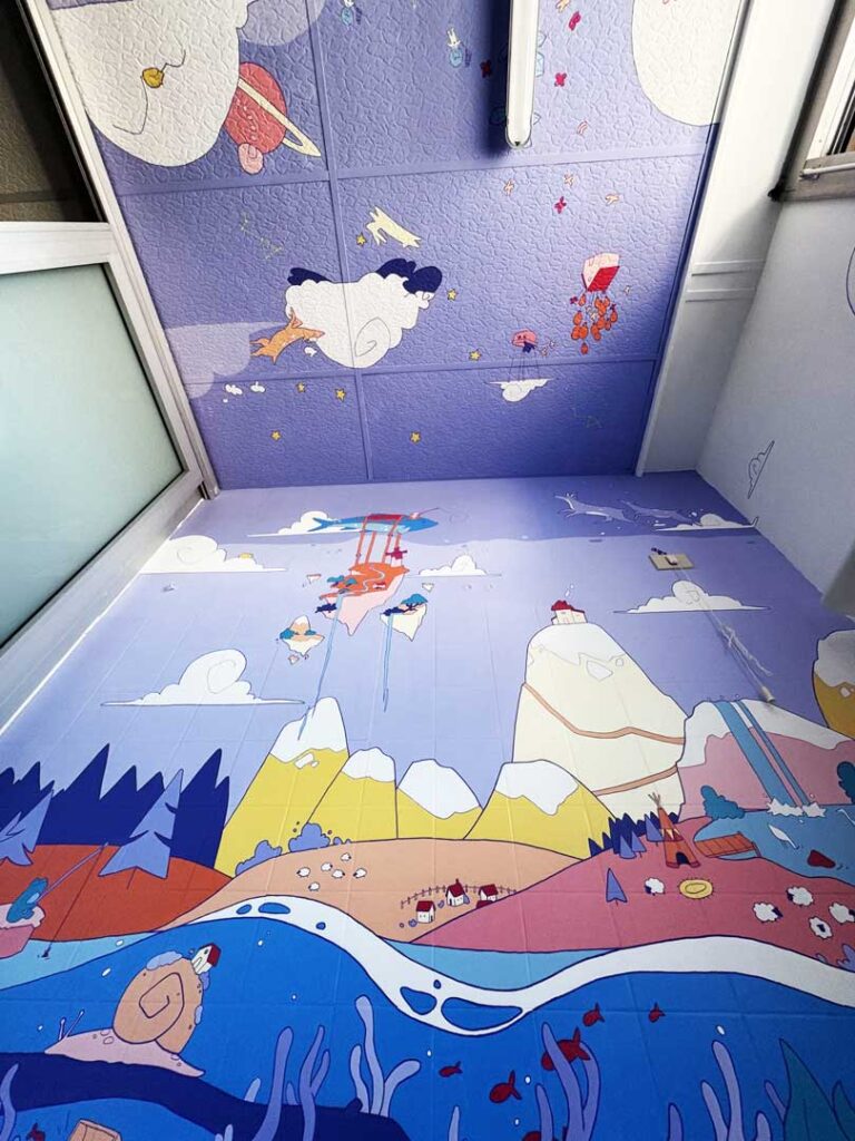 Fresque colorée achevée dans une salle de bain du CHU de Montpellier, représentant un paysage imaginaire entre ciel, montagnes et monde marin.