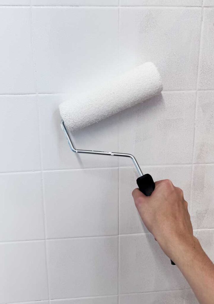 Application de peinture blanche au rouleau sur un mur carrelé avant la création de la fresque du CHU de Montpellier.